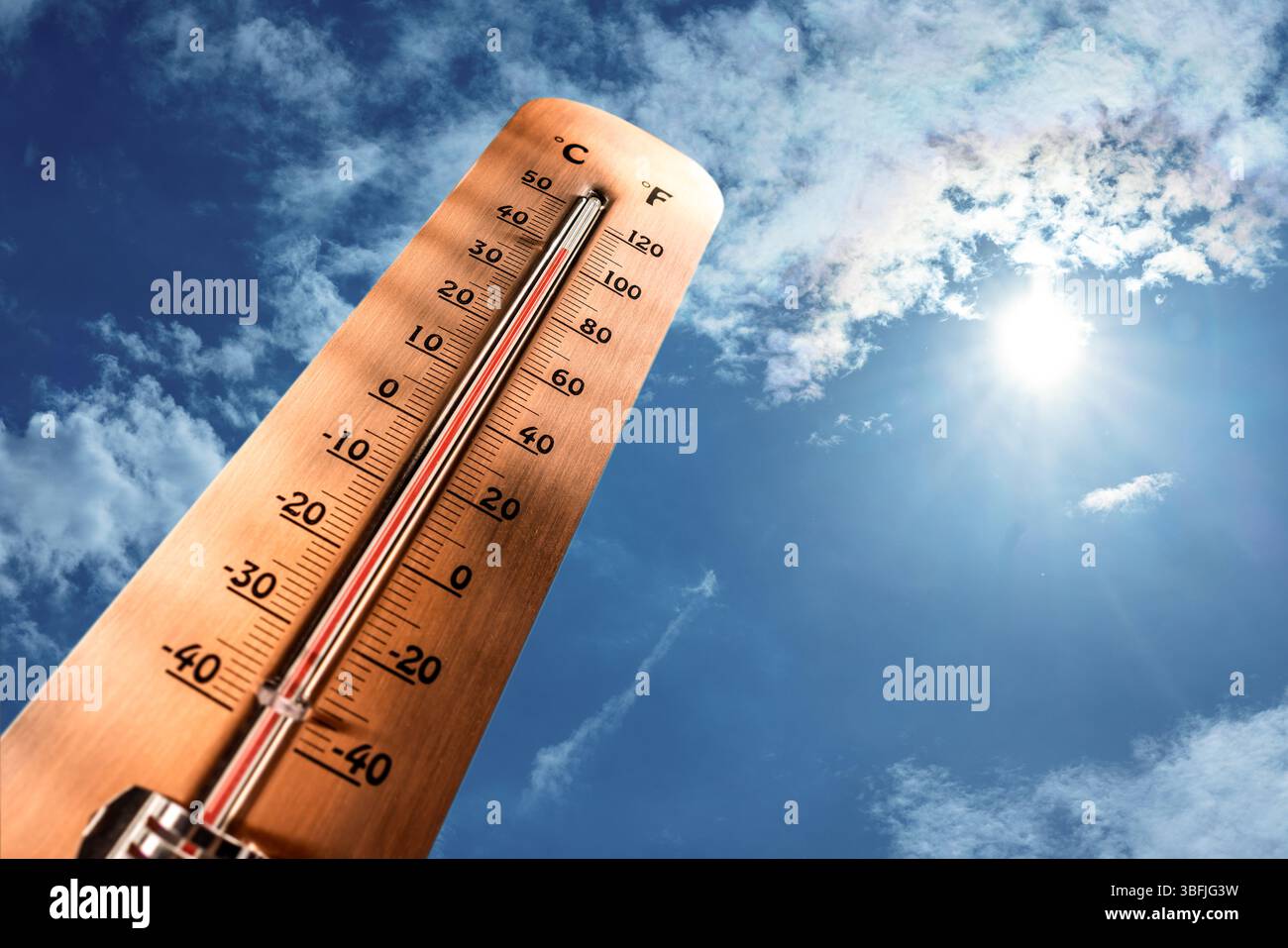 Thermometer showing tropical heat and sky with hot sun rays in Celsius and Fahrenheit. Stock Photo