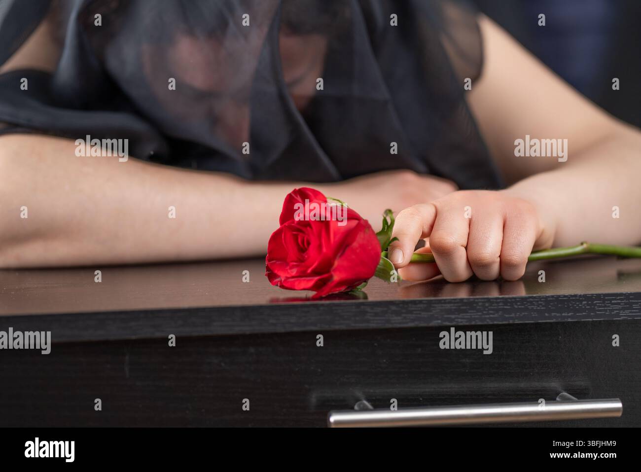 Woman crying over a coffin at a funeral with a red rose in her hand ...
