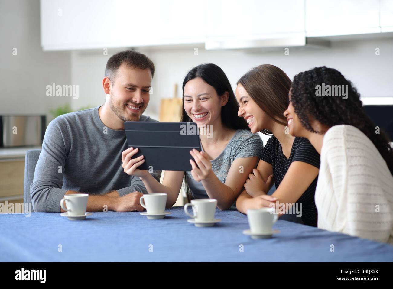 Happy interracial friends are checking tablet in a kitchen at home Stock Photo