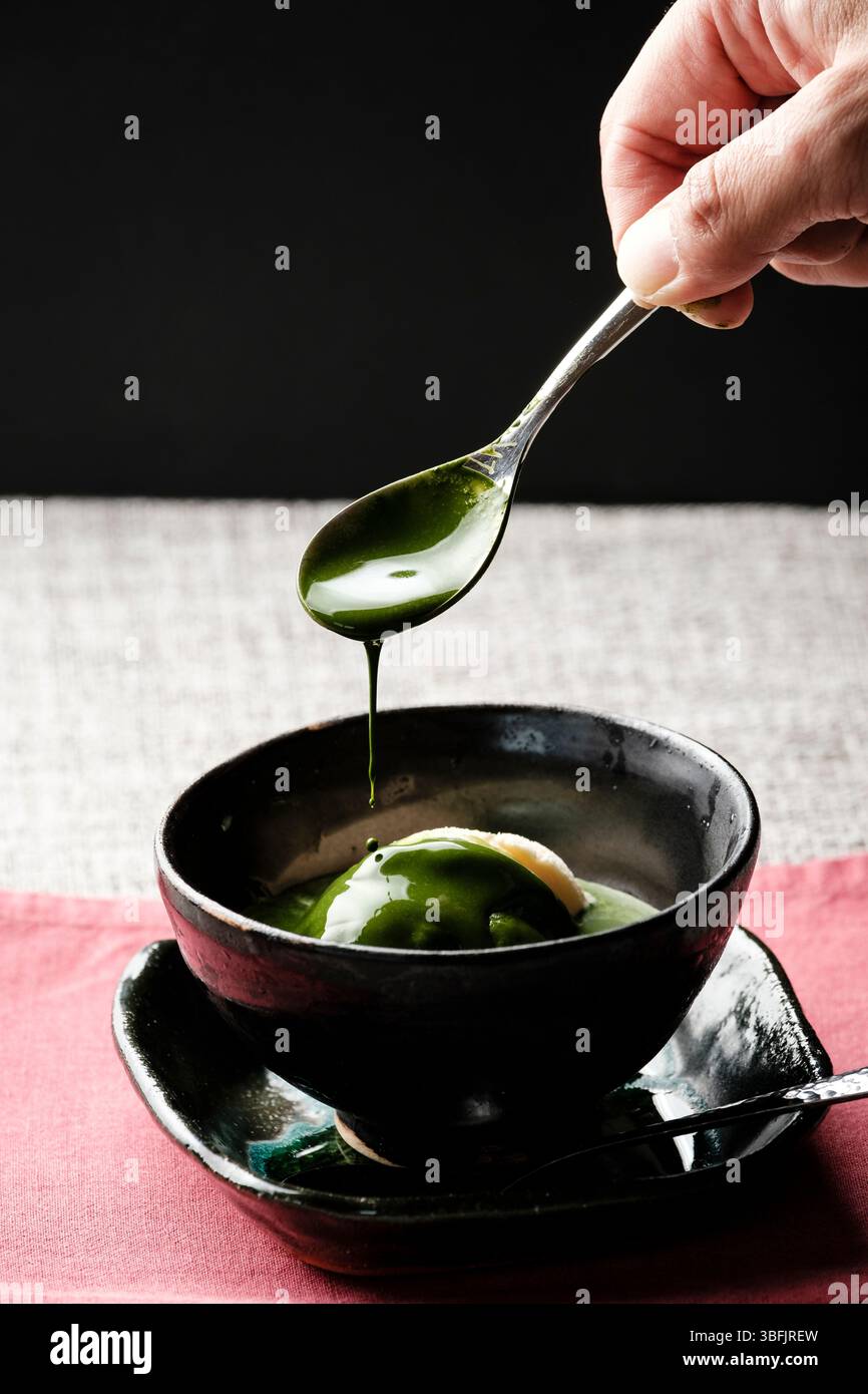 Hand dripping matcha sauce on vanilla ice cream Stock Photo