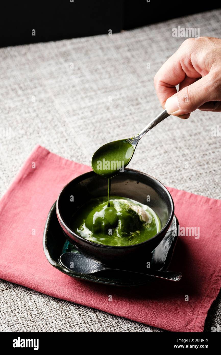 Hand dripping matcha sauce on vanilla ice cream Stock Photo