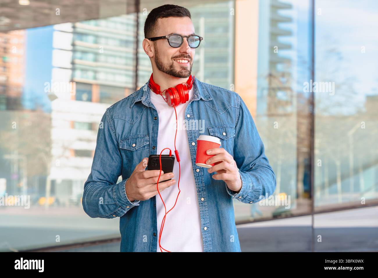 Smiling man using smartphone and holding coffee cup in modern urban setting Stock Photo