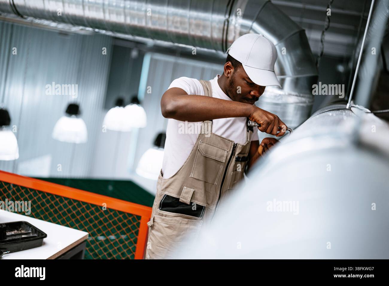 Worker performs maintenance on ventilation system in modern industrial space during daylight hours Stock Photo