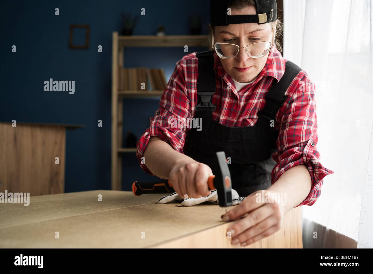 Woman in work overalls using hammer and nails for furniture assembly ...