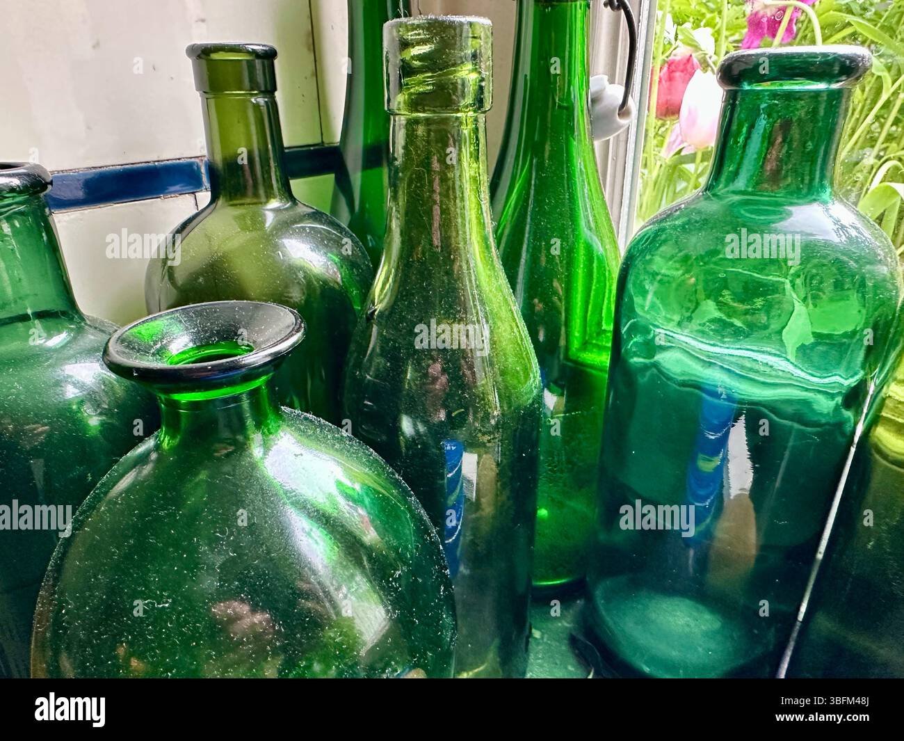 An assortment of green vintage glass bottles next to a window - Smartphone Captured Stock Image