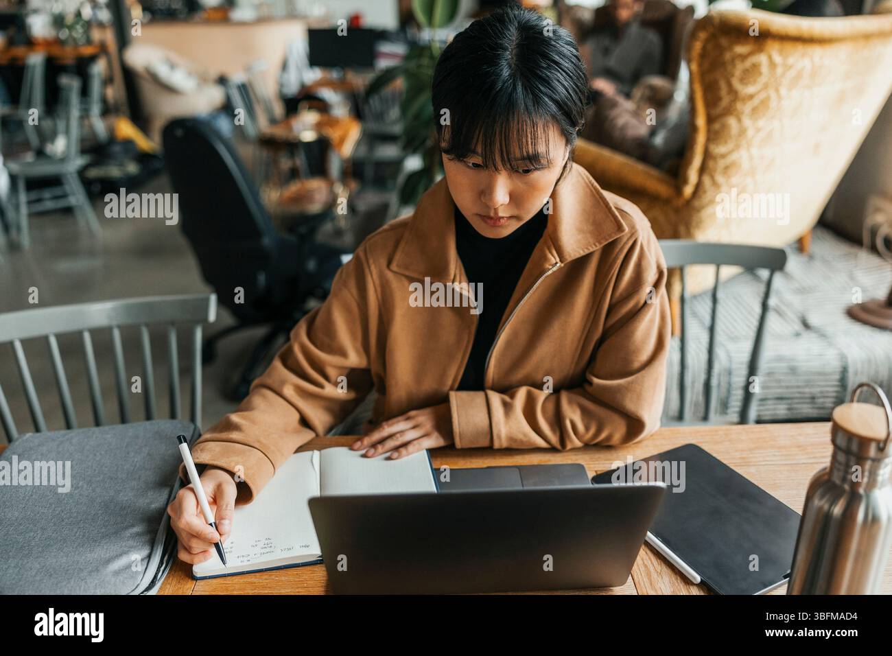 Focused young businesswoman with bangs taking down notes in diary at office Stock Photo