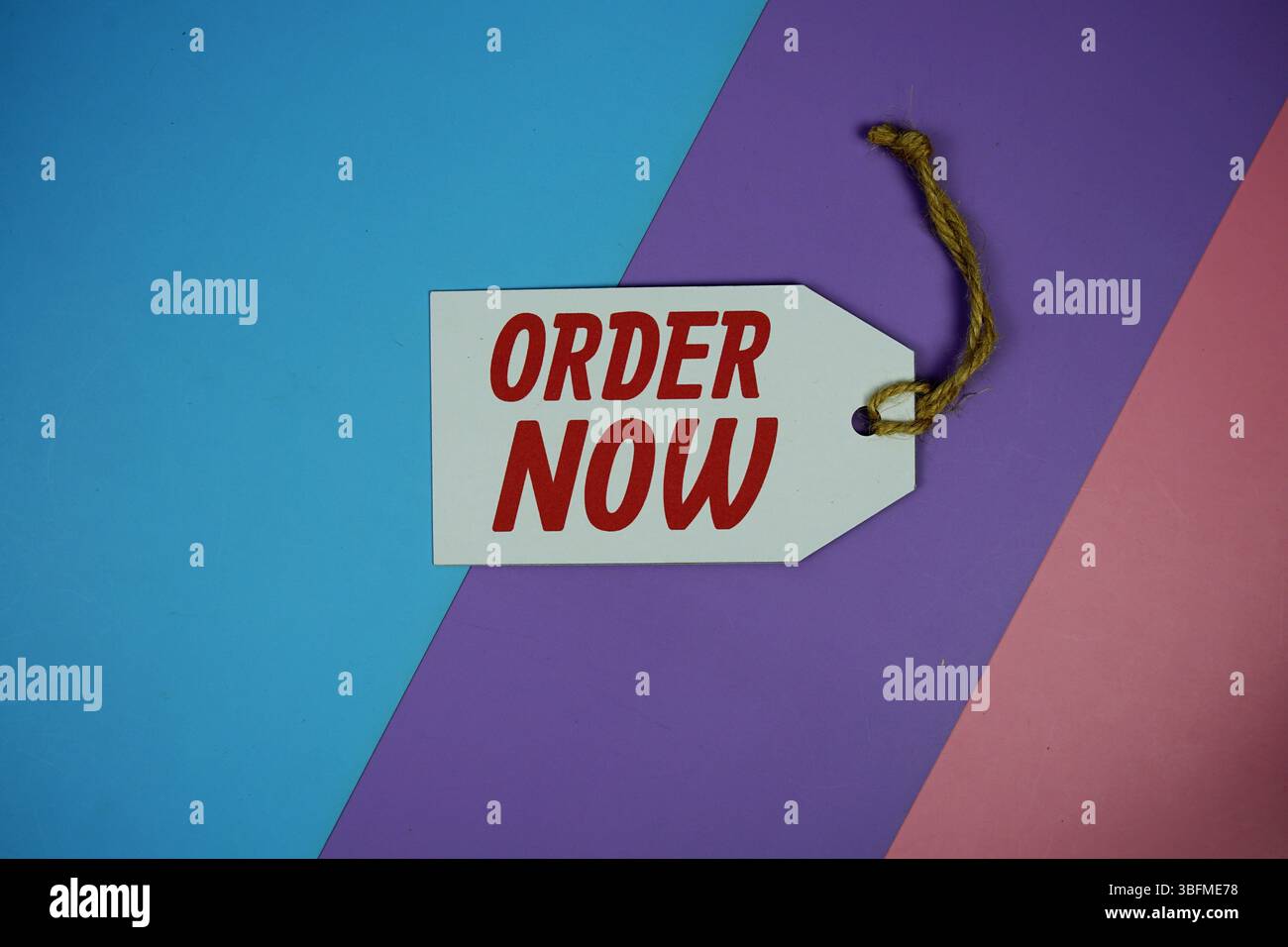Order Now text on price tag top view on purple geometric background Stock Photo