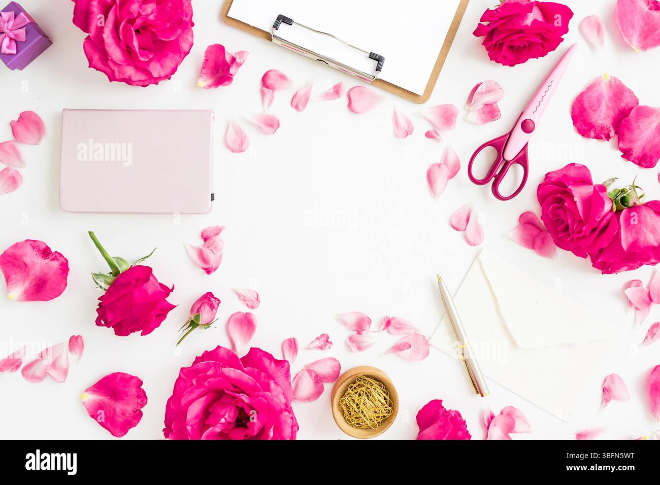 Creative workspace flat lay with pink roses, petals, notebook, scissors, and envelope on white background. Stock Photo