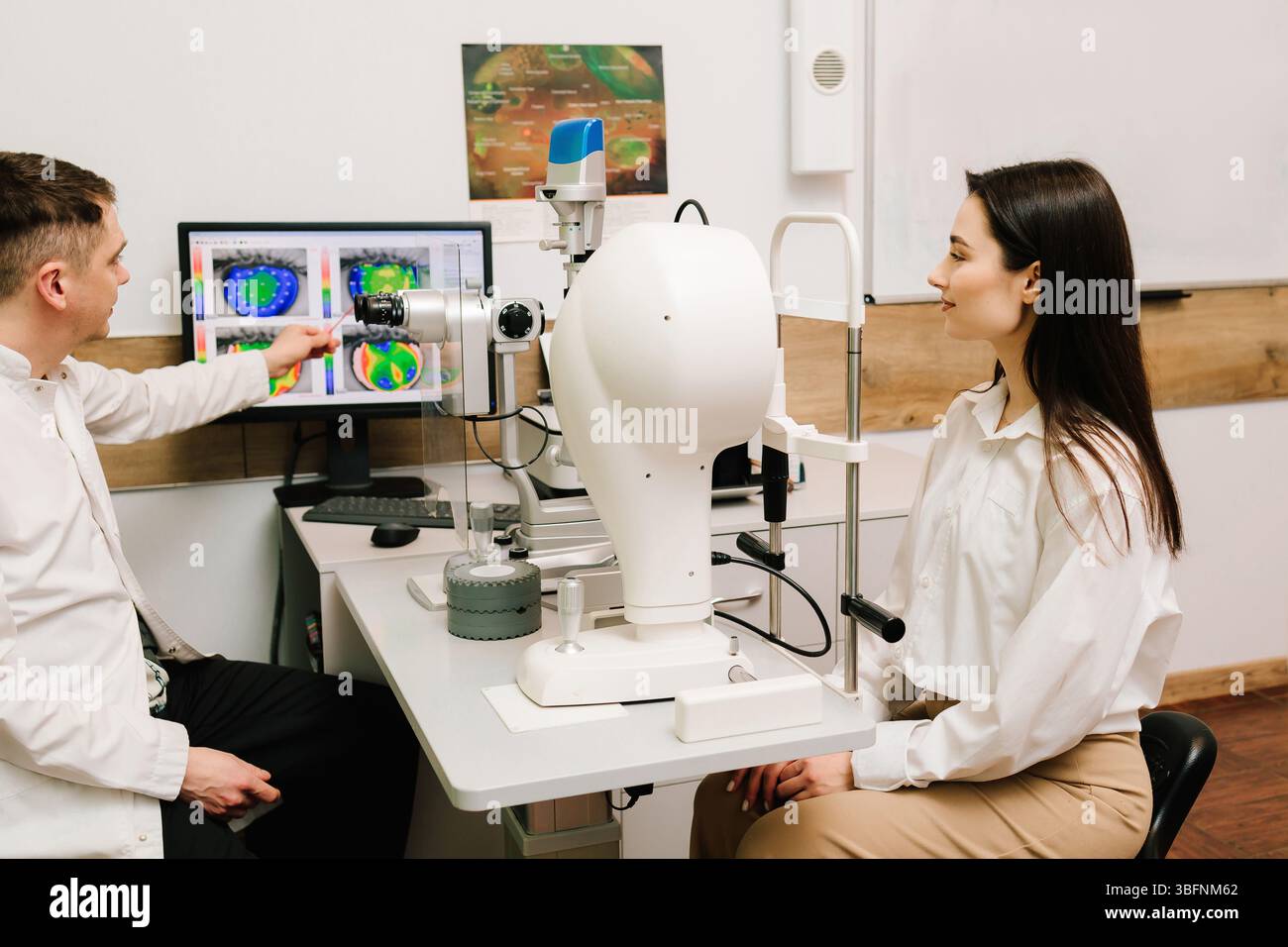 Topography Scan Ophthalmologist is showing corneal topography scan to girl patient near ...