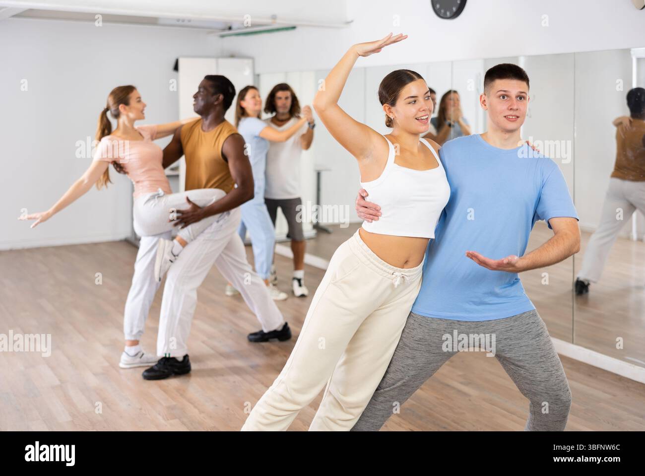 Smiling young adult couples dancing together in pairs and practicing new movements in modern studio Stock Photo
