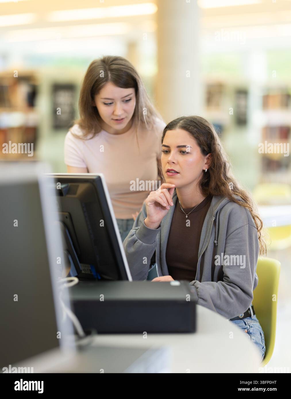 Two female students near the monitor in the library Stock Photo - Alamy