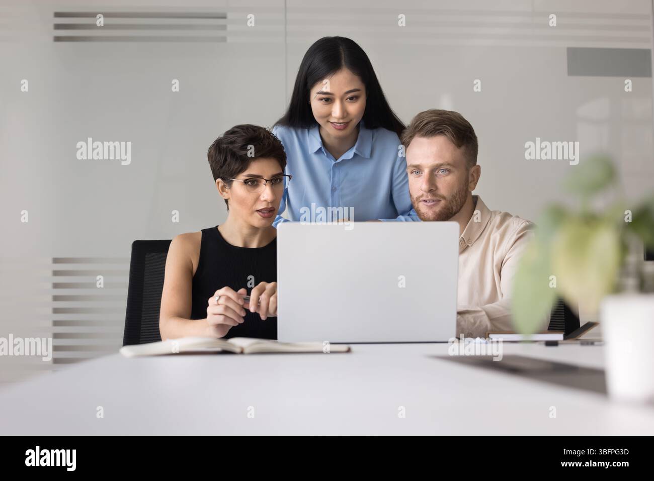 Three teammates using laptop engaged in teamwork in modern office Stock Photo