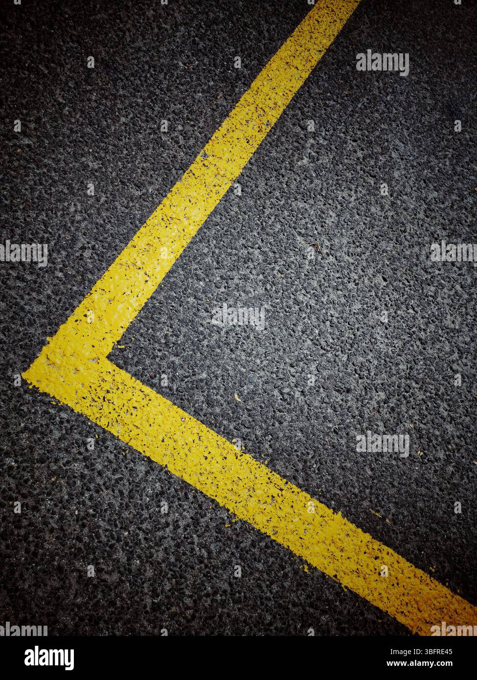 Bright yellow line marking outlines the dimensions of a parking space on a dark asphalt surface in an urban setting - Smartphone Captured Stock Image