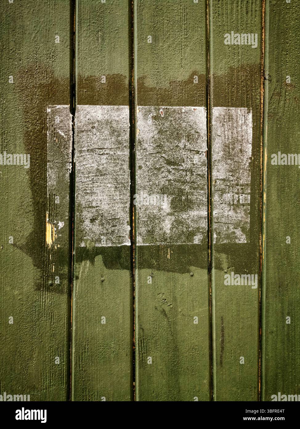 A rectangular patch on a green wooden surface shows faded remnants of a past application, with chipped paint revealing the wood grain. - Smartphone Captured Stock Image