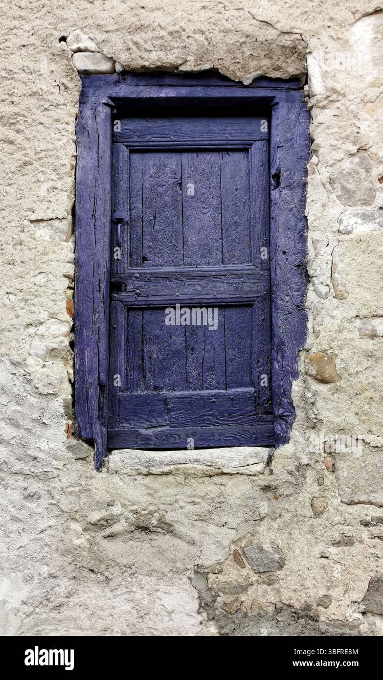 A small door painted in vibrant purple contrasts beautifully with a weathered stone wall. - Smartphone Captured Stock Image