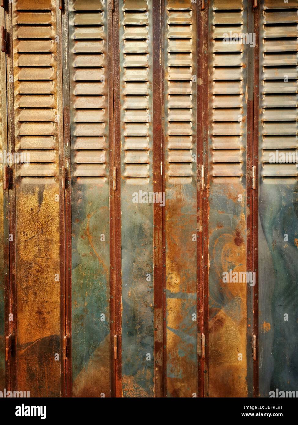 Rustic wooden shutters exhibit a blend of rusty and faded paint, showcasing years of weathering in an urban setting illuminated by natural light - Smartphone Captured Stock Image