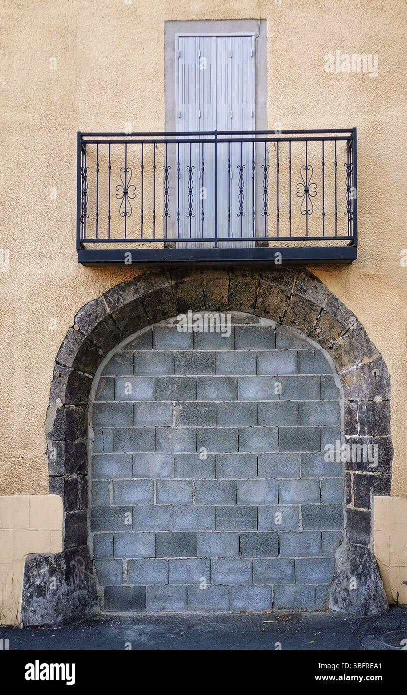 A metal-railed balcony stands over a blocked stone entrance on a textured yellow building, creating a striking architectural feature in an urban area. - Smartphone Captured Stock Image