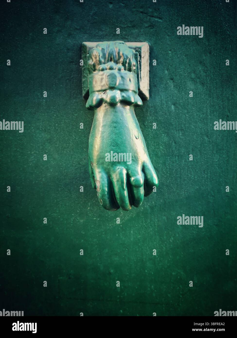 A unique green hand-shaped door knocker adorns a textured dark wall, adding a charming historical touch to the location. - Smartphone Captured Stock Image