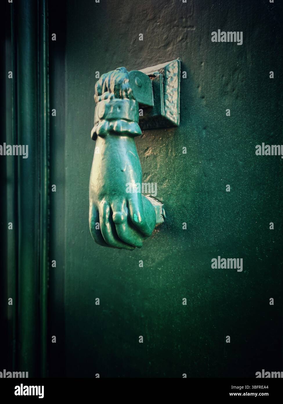 A distinctive bronze hand-shaped door knocker is mounted on a teal door - Smartphone Captured Stock Image