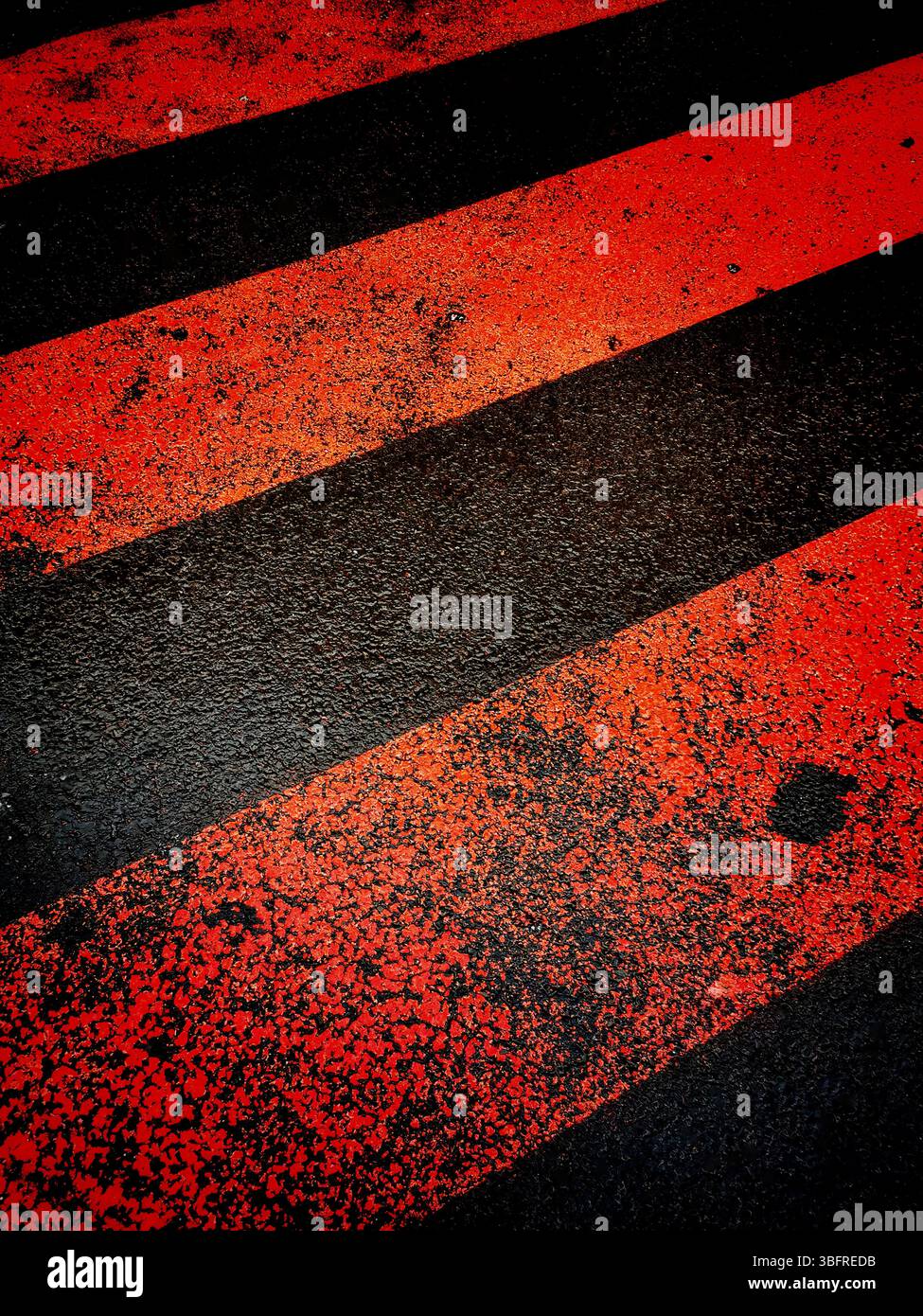 A bright red and black striped crossing painted on the asphalt - Smartphone Captured Stock Image
