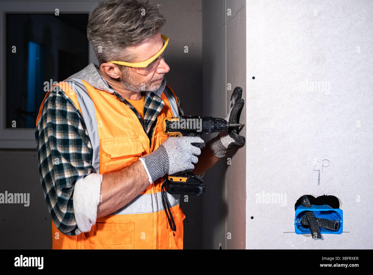 Electrician securing drywall with a cordless power drill. Wearing ...