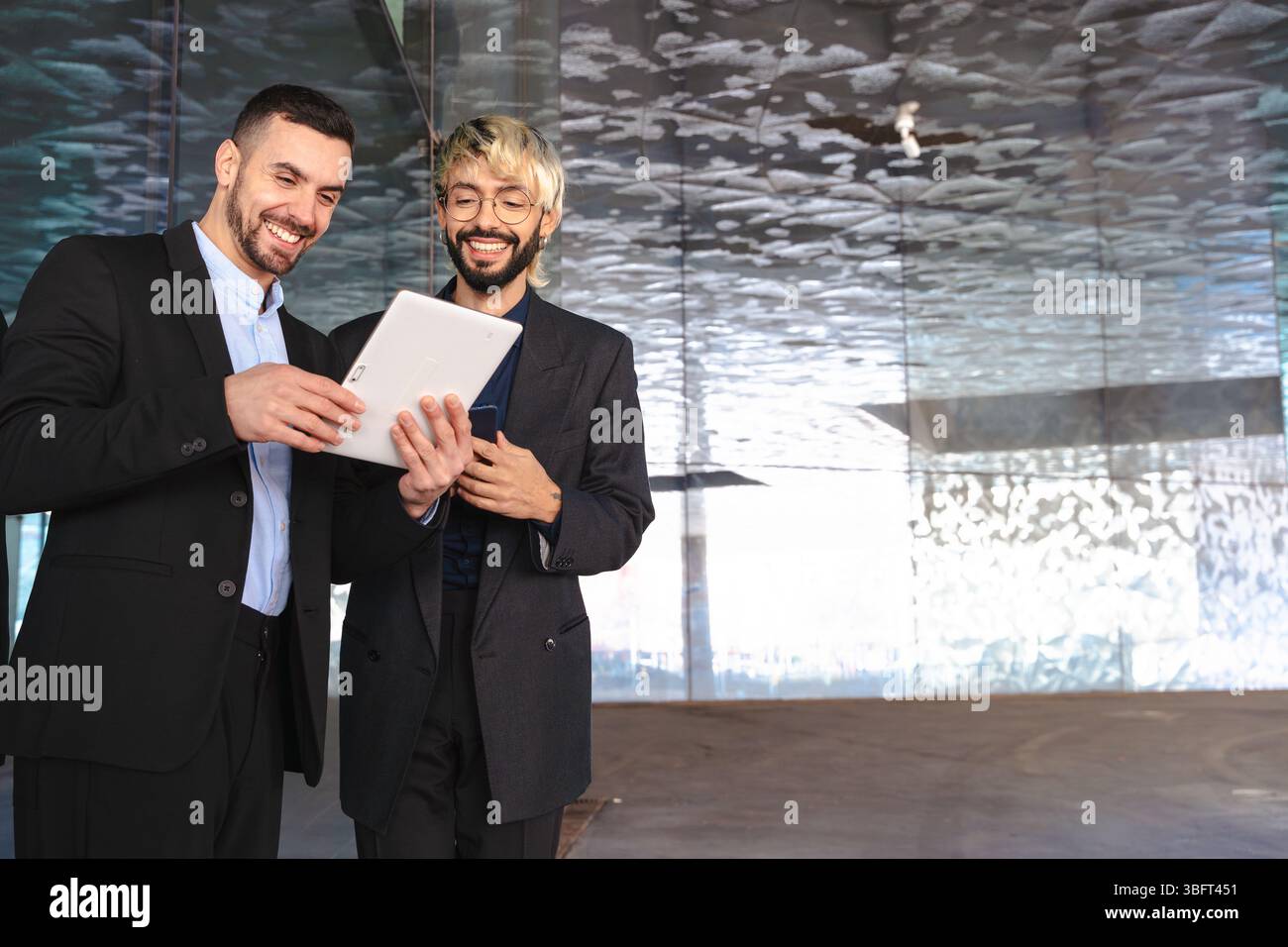 Two businessmen in suits using tablet together and smiling in modern ...