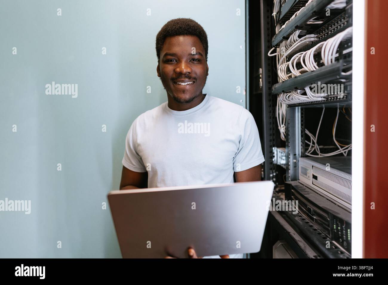 Young technician working in server room, managing cables and technology efficiently while smiling Stock Photo