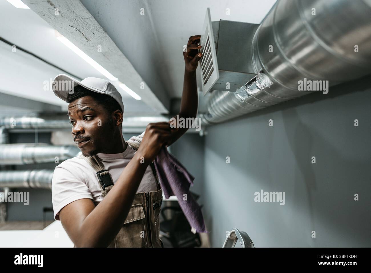 Worker performs maintenance on ventilation system in commercial building during daytime hours Stock Photo