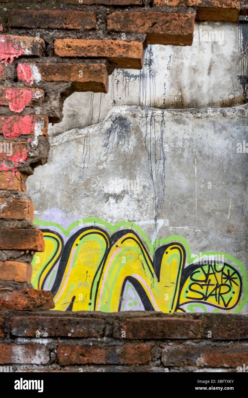 Bali, Indonesia - Dec 10, 2024: Wall with graffiti on it and a hole in it. The graffiti is mostly yellow and blue Stock Photo