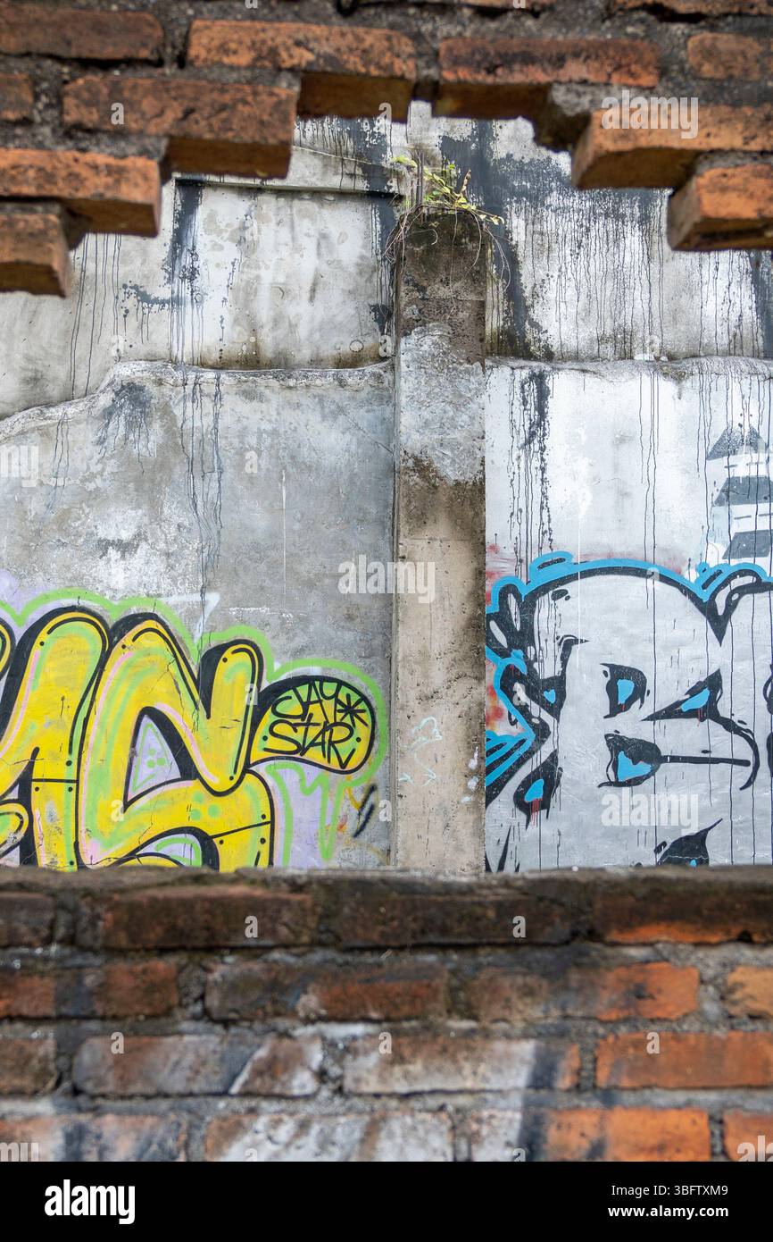 Bali, Indonesia - Dec 10, 2024: Wall with graffiti on it and a hole in it. The graffiti is mostly yellow and blue Stock Photo