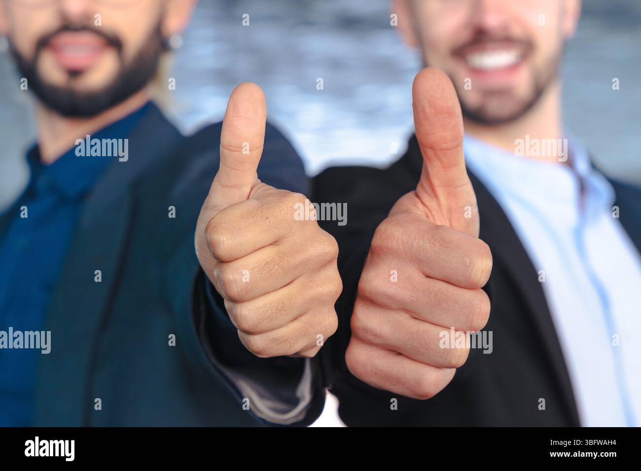 Two confident businessmen in suits giving thumbs up and smiling at camera Stock Photo