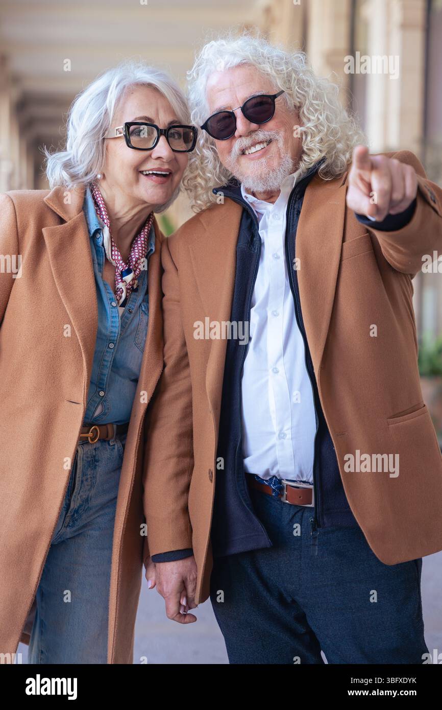 Happy senior couple outdoors, man pointing and smiling at the camera.Vertical Stock Photo