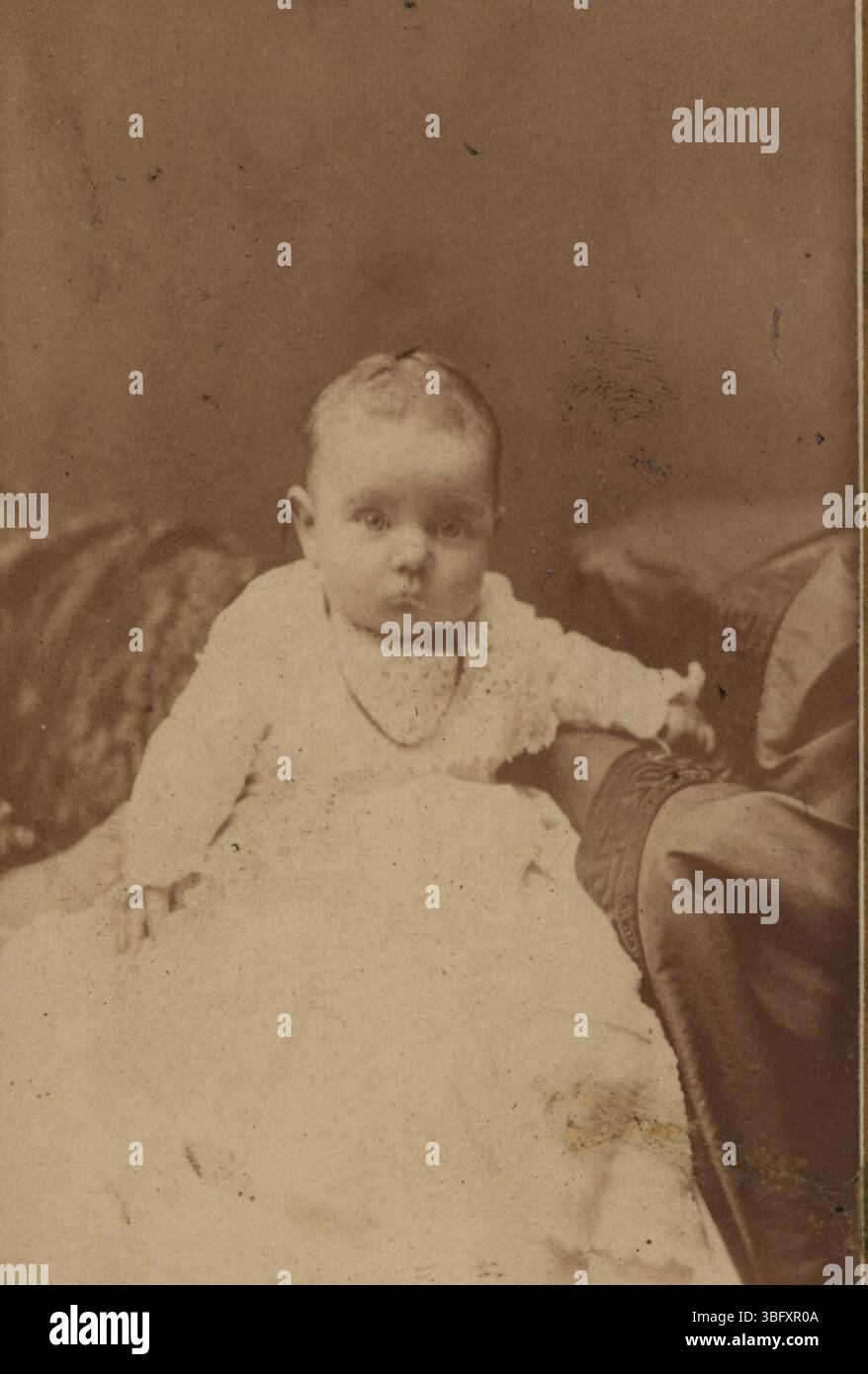 This 1876 photograph from the Miller Family Collection shows an unidentified baby dressed in Victorian attire. The baby's identity is unknown, as the photograph's back provides no further information. Stock Photo