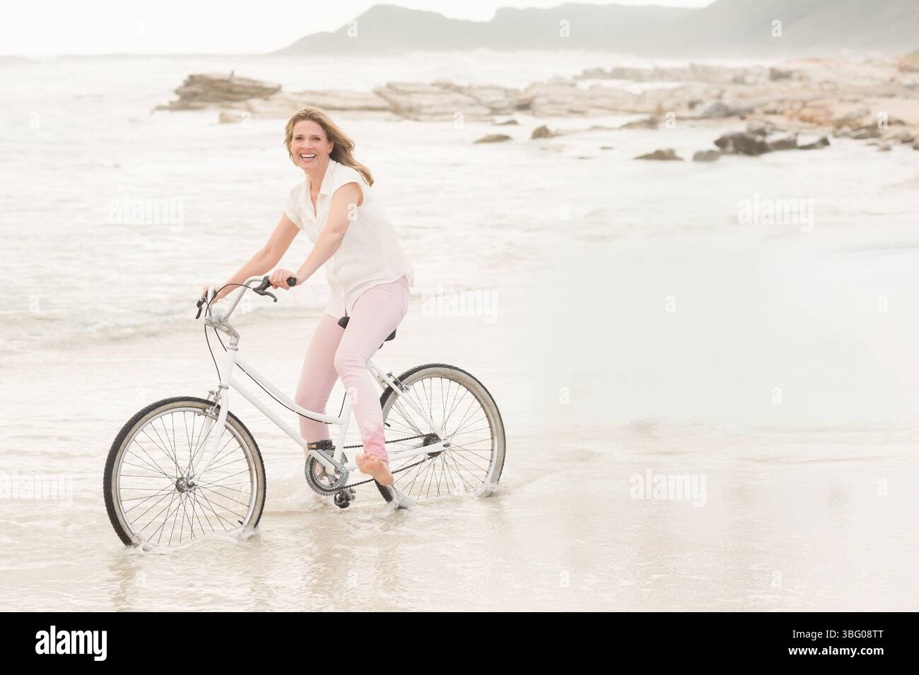Woman riding white cruiser bicycle through shallow water along wet ...