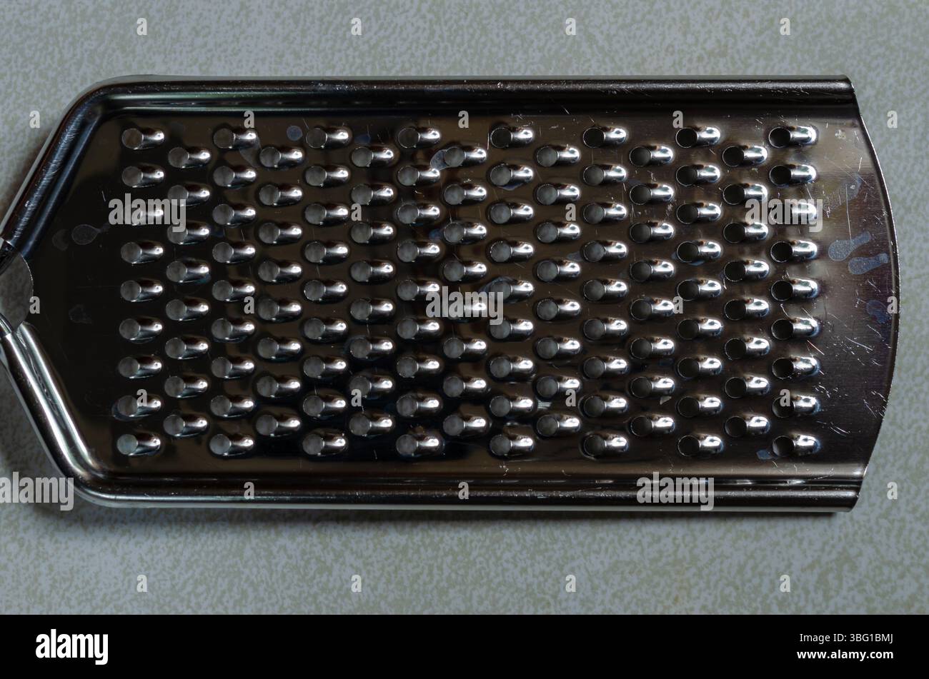 Hand held steel cheese grater on a gray patterned background Stock Photo