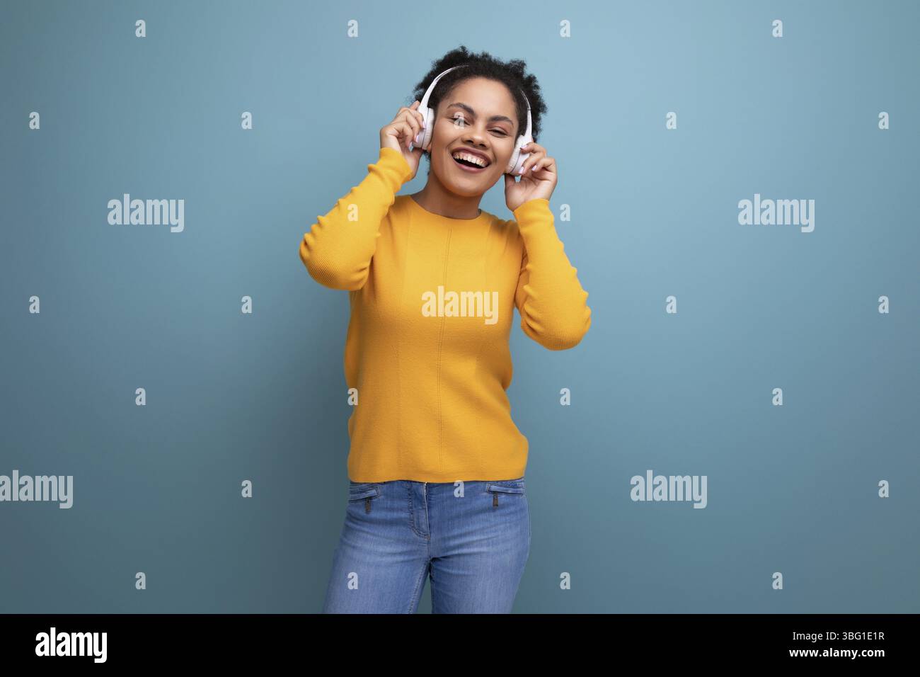 Cheerful young hispanic business woman with black curly hair listening to music in white headphones Stock Photo