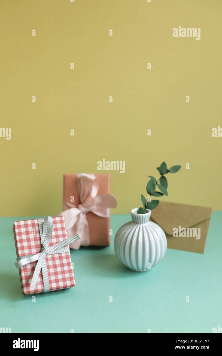 Gift box, plant, envelope on green table. yellow wall background Stock Photo
