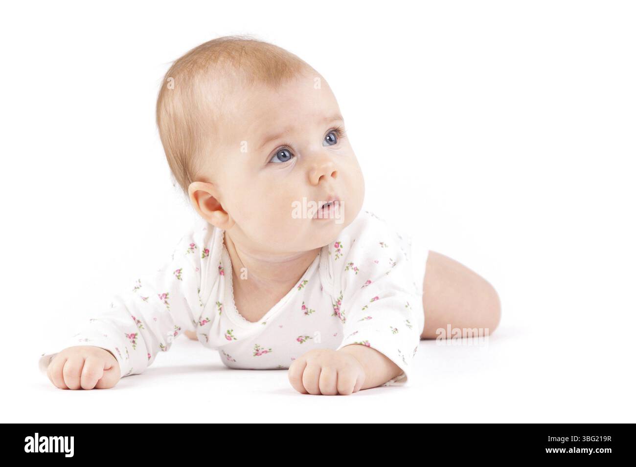 Isolated on white, cute baby girl in white pijamas lies on belly, sad, look at right Stock Photo
