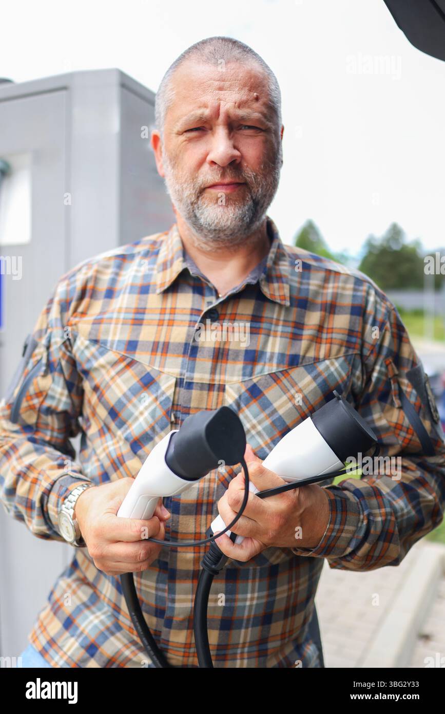Adult man refueling electric vehicle at charging point. Green tech and future mobility. Stock Photo