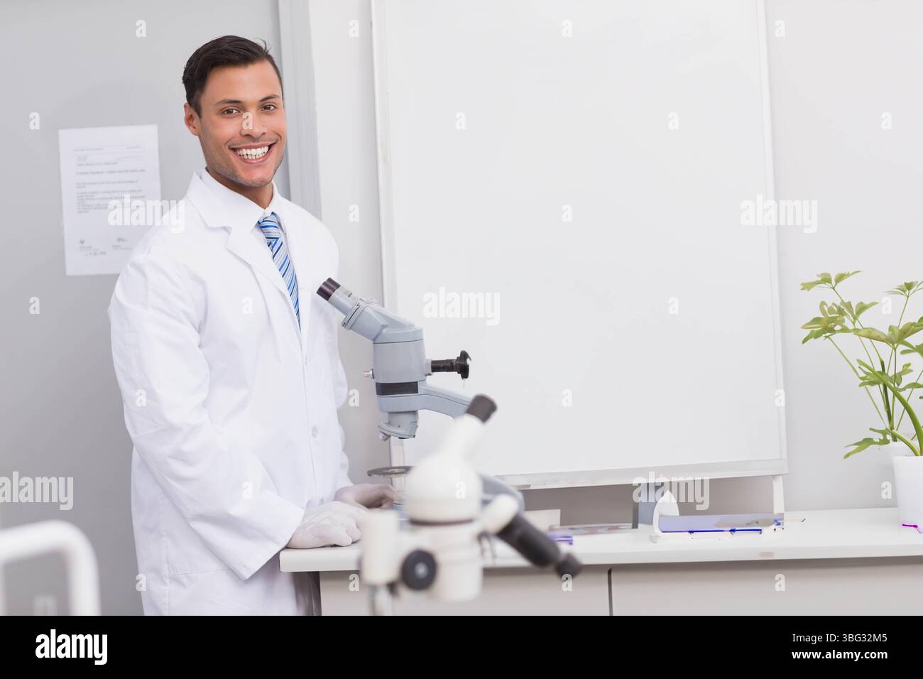 Male researcher standing at lab bench wearing lab coat, gloves ...
