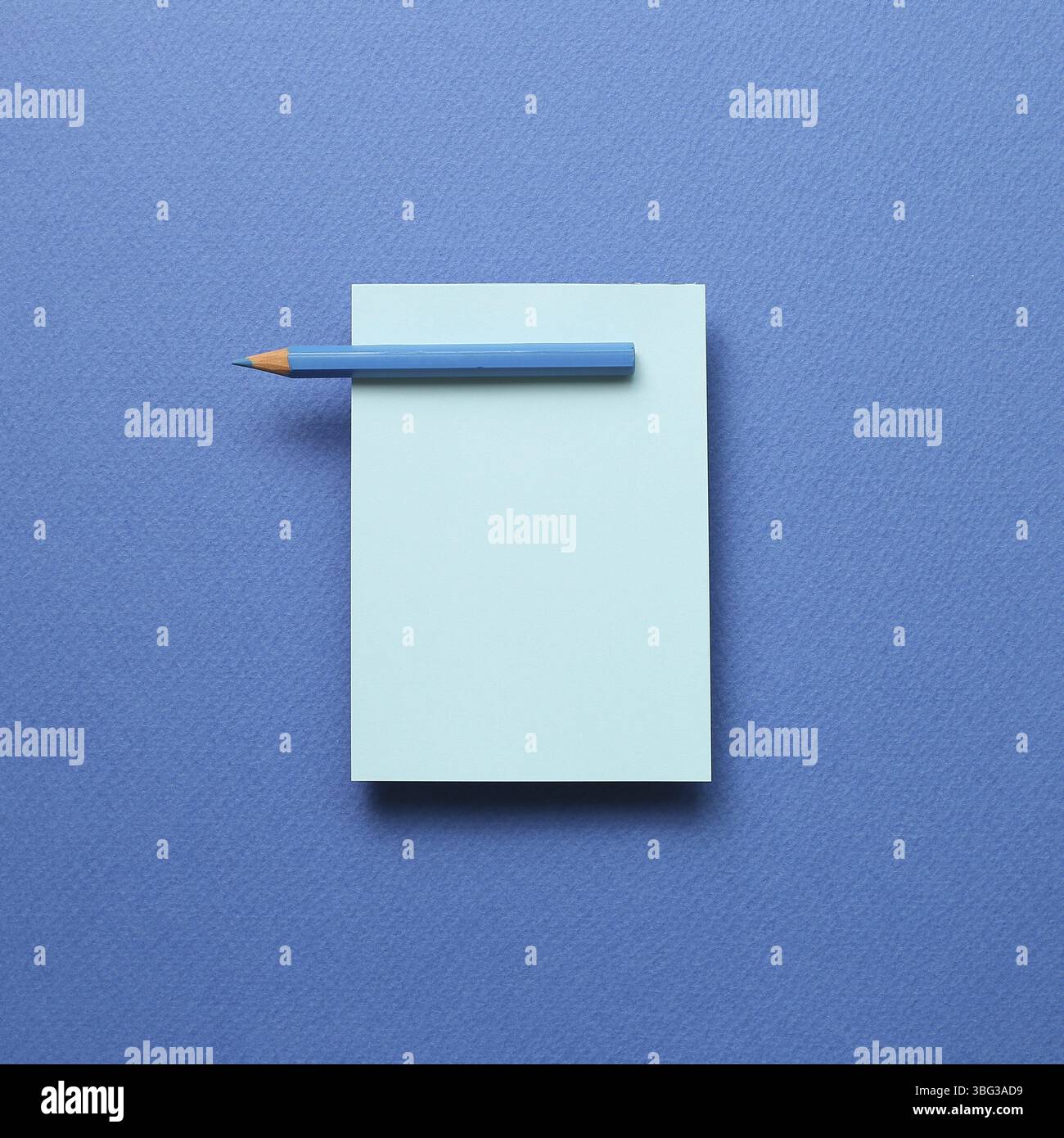 Blue memo note pad and blue colored pencil on blue background Stock Photo