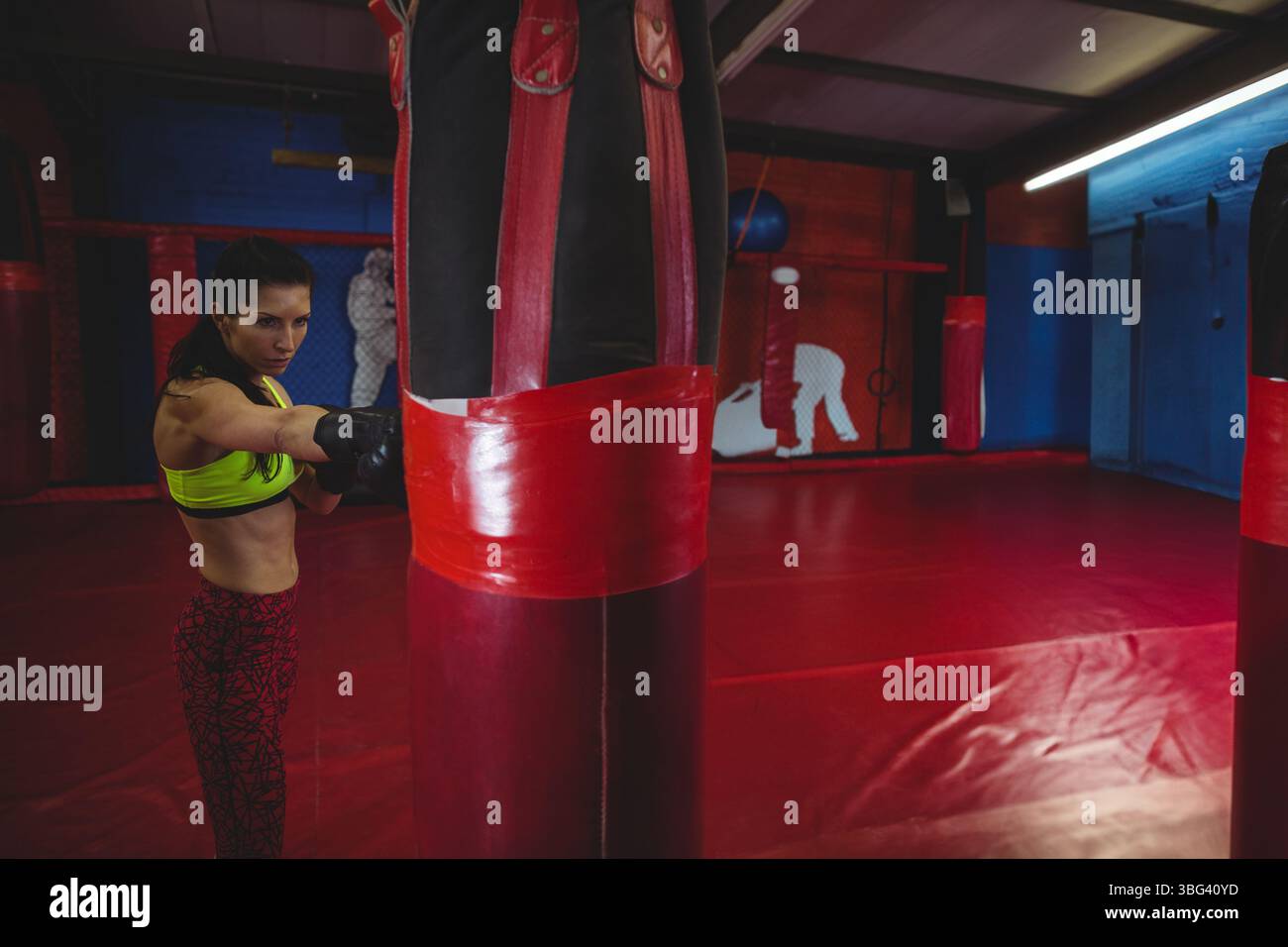 Woman punching heavy bag in martial arts gym wearing sports bra and gloves, copy space Stock Photo