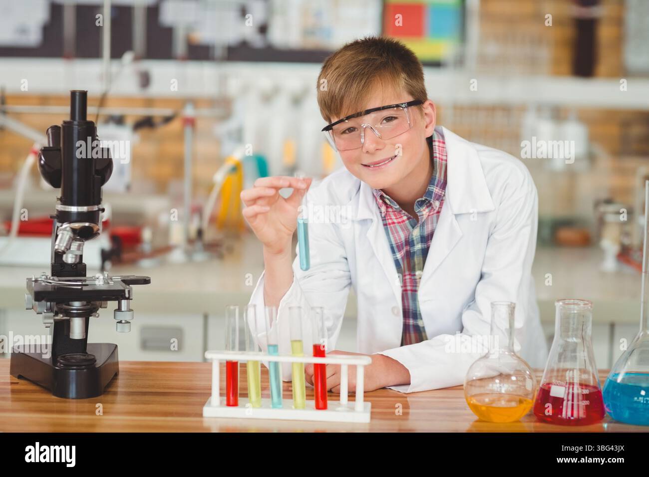 Boy wearing safety goggles and lab coat, examining test tube rack ...
