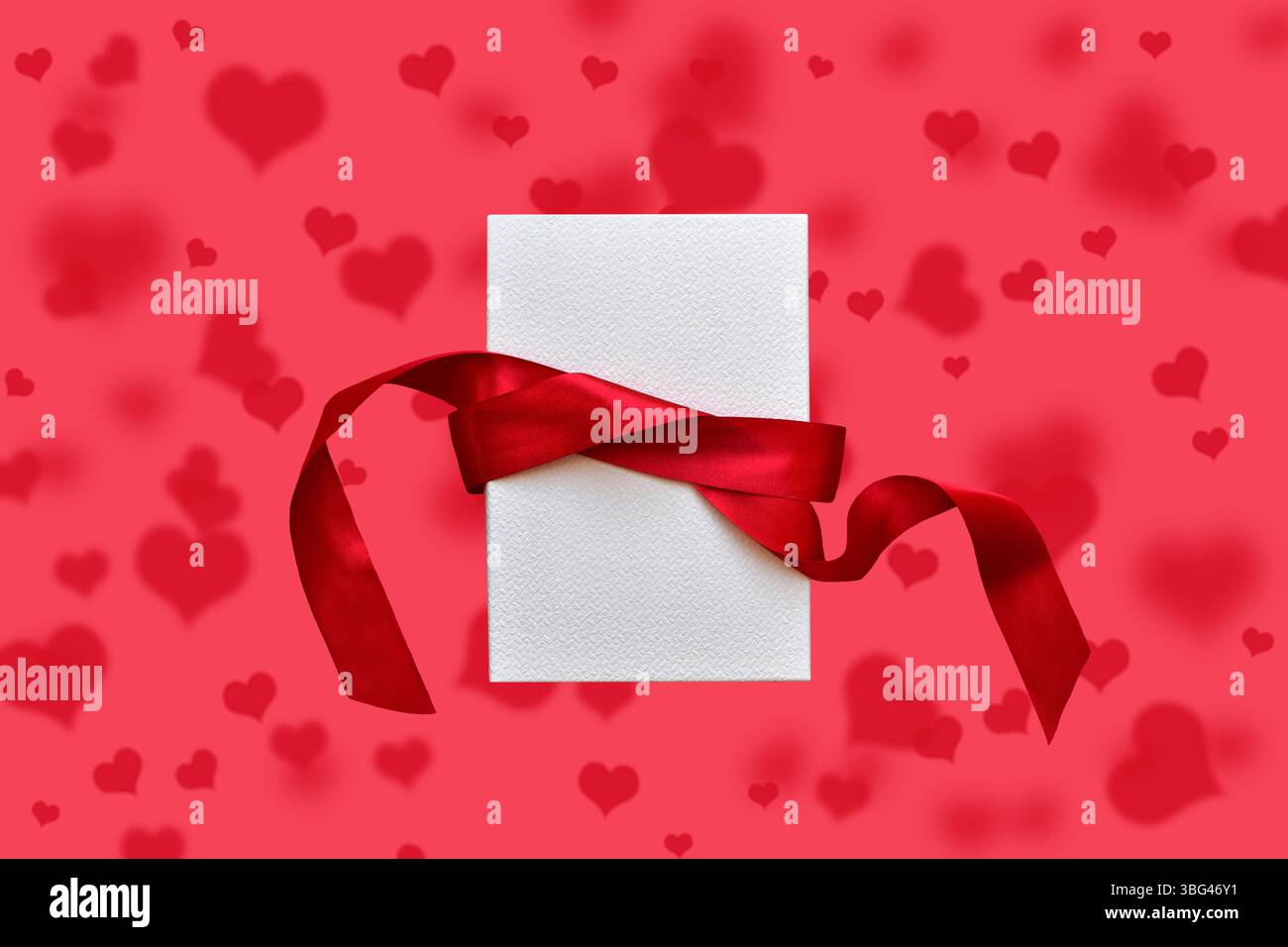 White gift box with red ribbon on red hearts pattern background Stock Photo