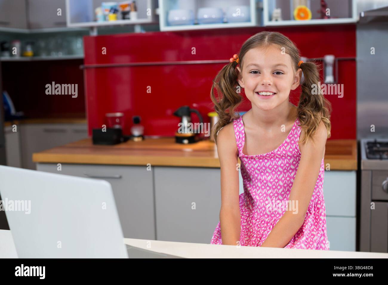 Girl leaning against counter in kitchen wearing pink dress and using ...