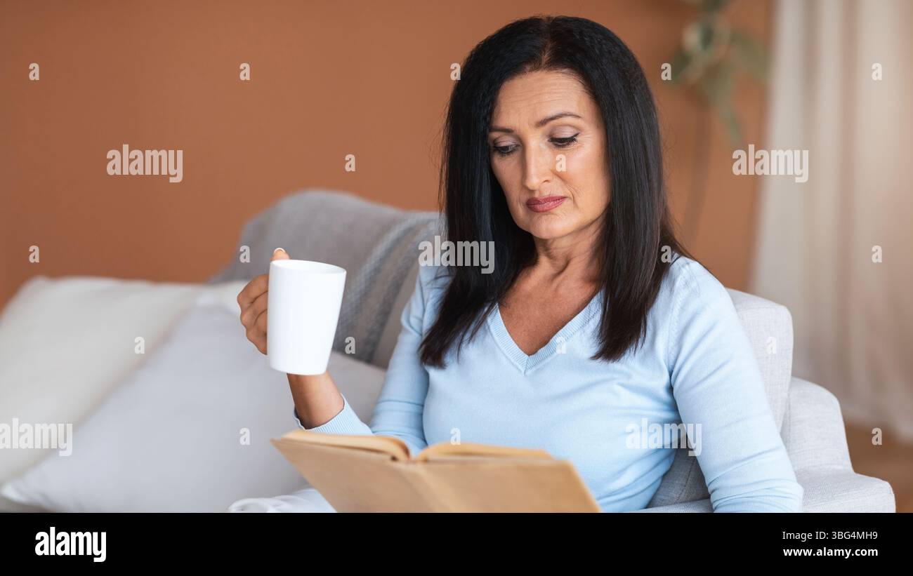 Mature lady reading book and holding cup of coffee Stock Photo