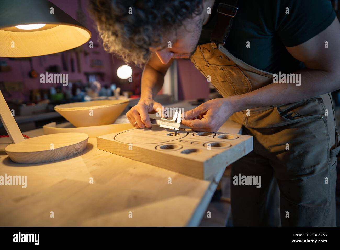 Concentrated woodworker check lamp components with caliper, prepared patterns for production on desk Stock Photo