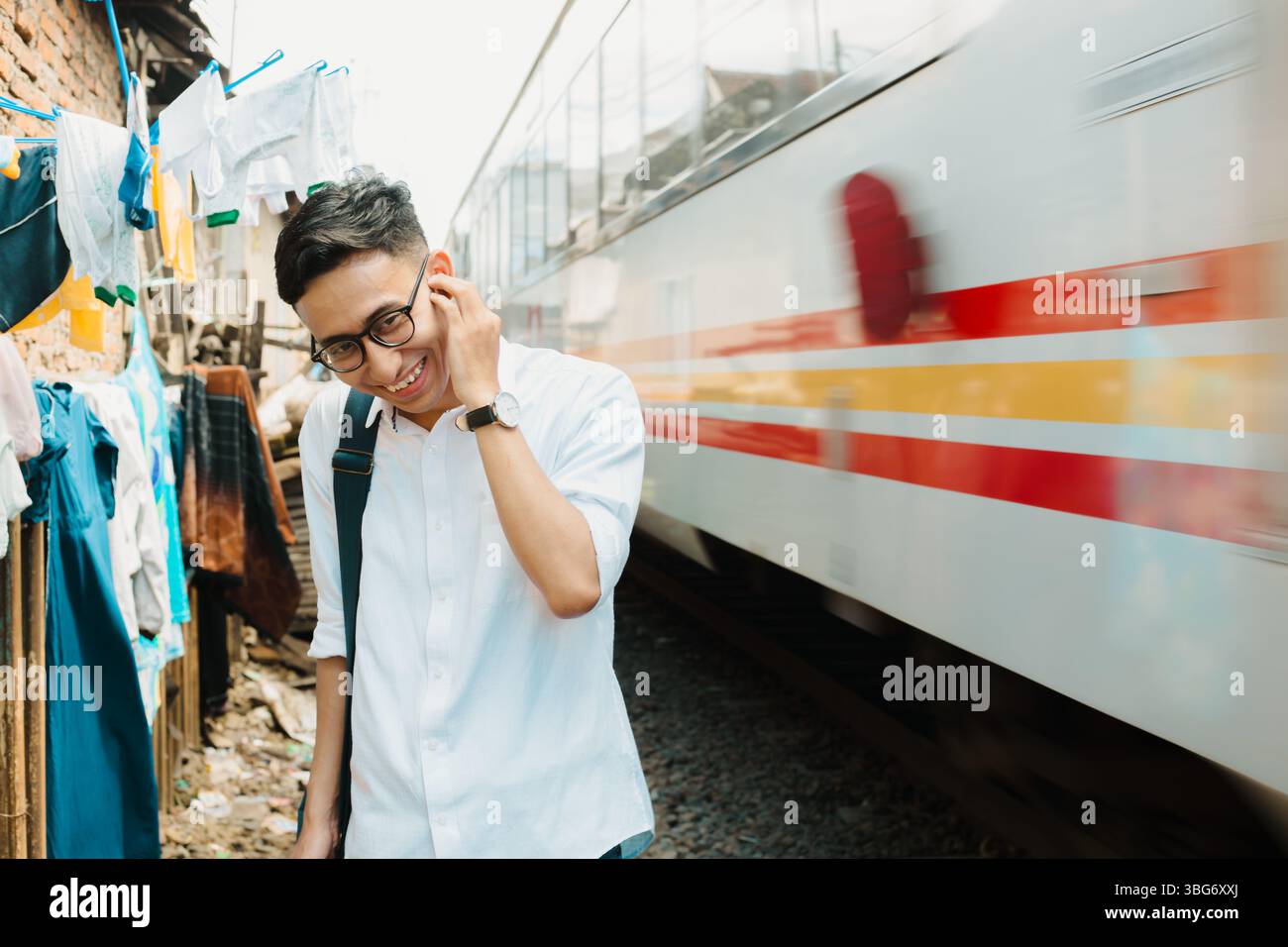 A smiling Indonesian traveler reacts to a passing train in Malang, capturing the energy of local transportation in Southeast Asia Stock Photo