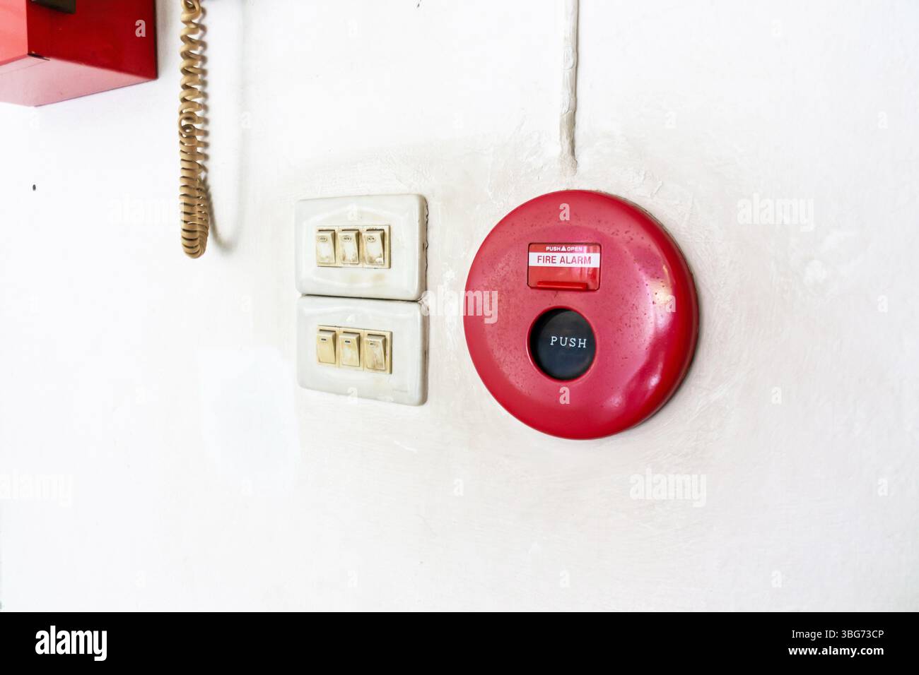 This image features a red fire alarm button mounted on a white wall ...
