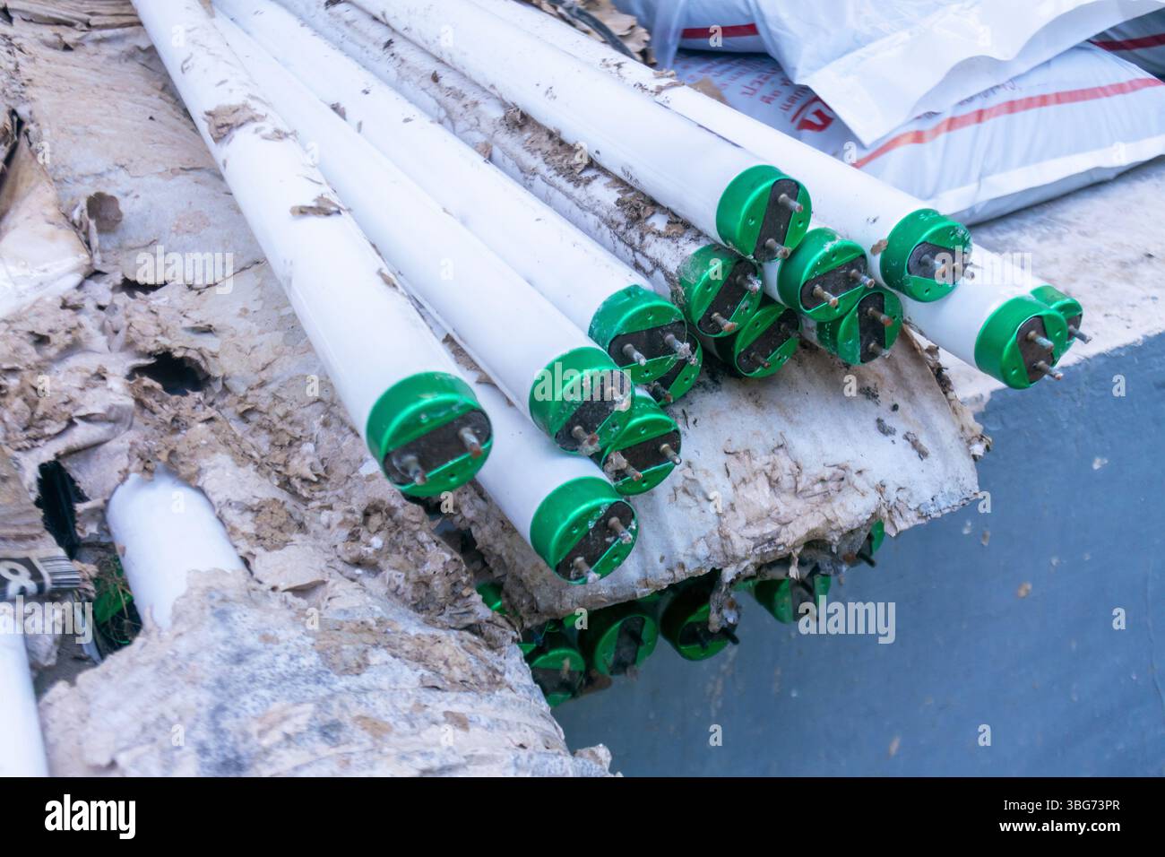 A collection of stacked fluorescent light tubes with green ends rests ...